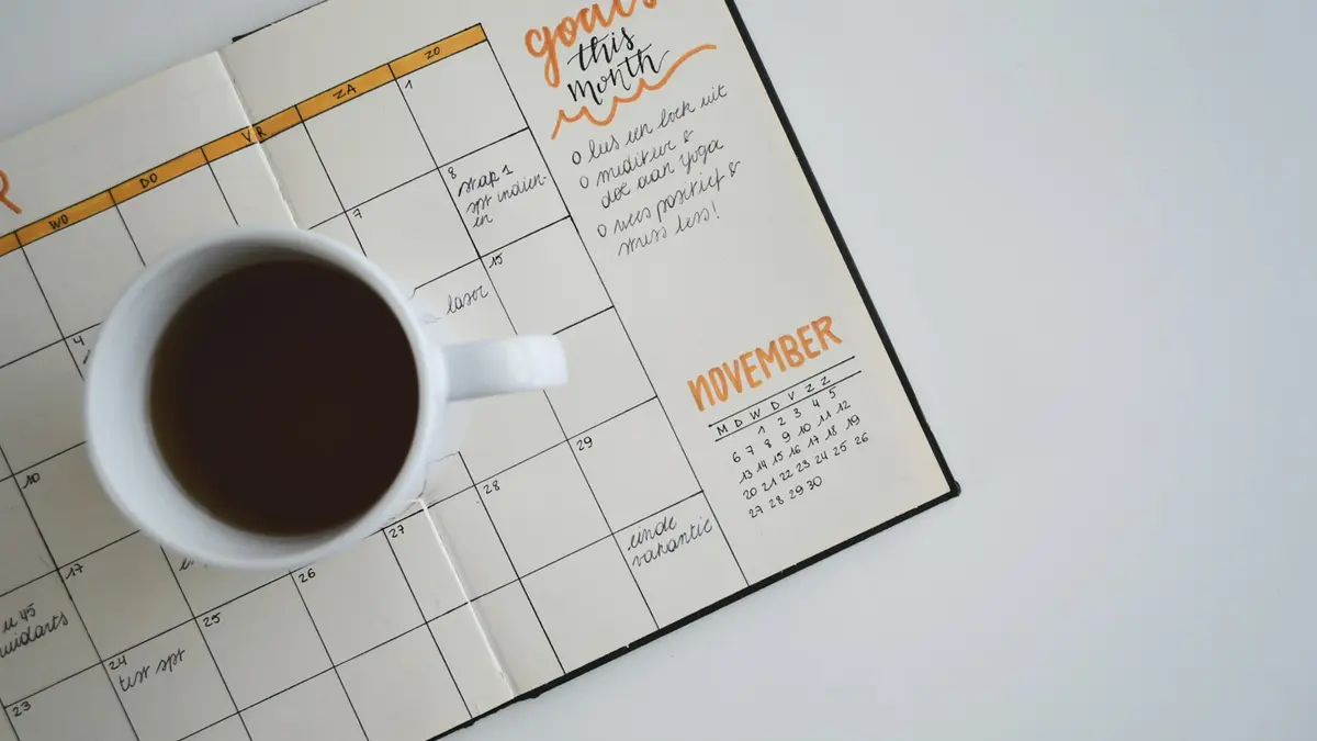 An open paper calendar on a desk next to a cup of coffee