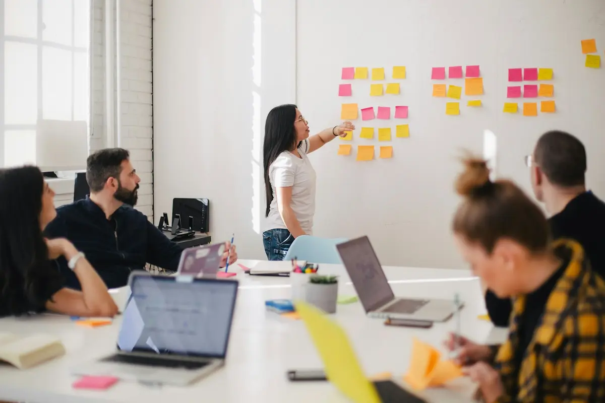 A team around a table with laptops and a wall of sticky notes
